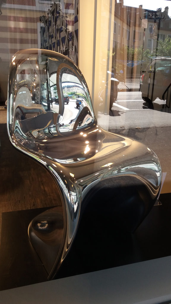 Design-Stuhl der Marke Panton, aufgenommen durch das Schaufenster mit Spiegelung der Umgebung